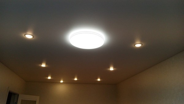 Простой белый-матовый натяжной потолок с точечными светильниками и люстрой в однокомнатной квартире